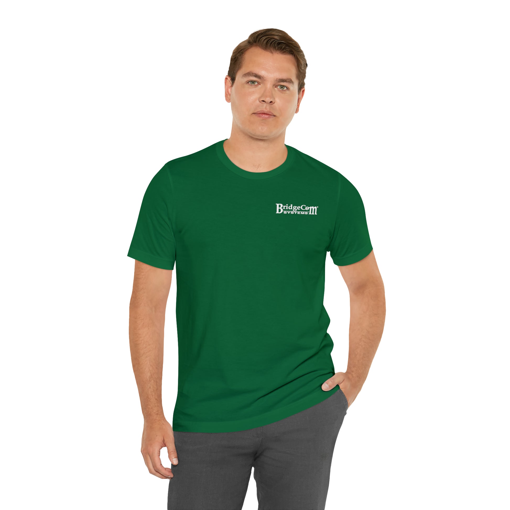 A person with short brown hair is wearing the "Short Sleeve Tee - Small Logo" in green, made from Airlume combed cotton, and featuring the "BridgeMill Sixes Service Associates" logo on the upper left side. The individual has one hand in their pocket and is posing against a plain white background.