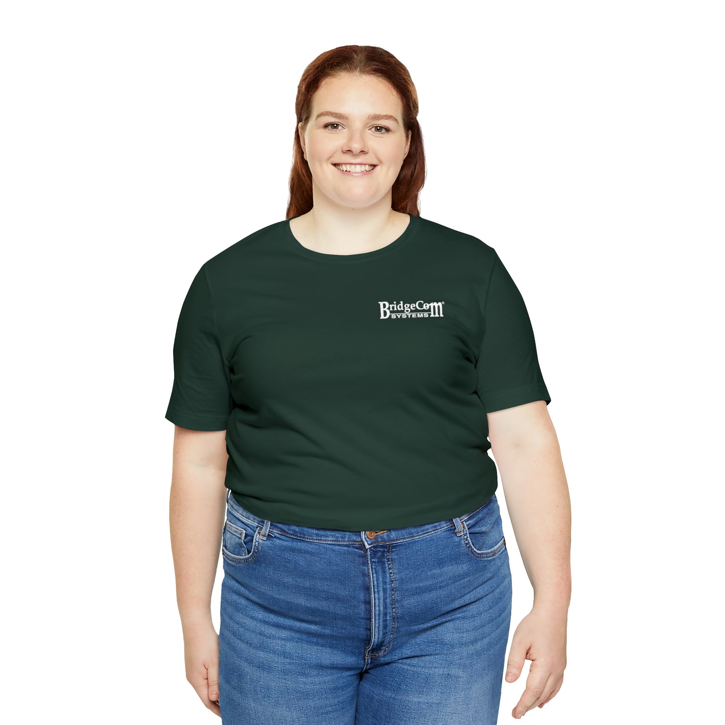 A woman with long red hair is smiling at the camera. She is wearing a dark green Short Sleeve Tee - Small Logo made from Airlume cotton, featuring the BridgeCom Systems logo on the upper left side, and blue jeans. The background is white.