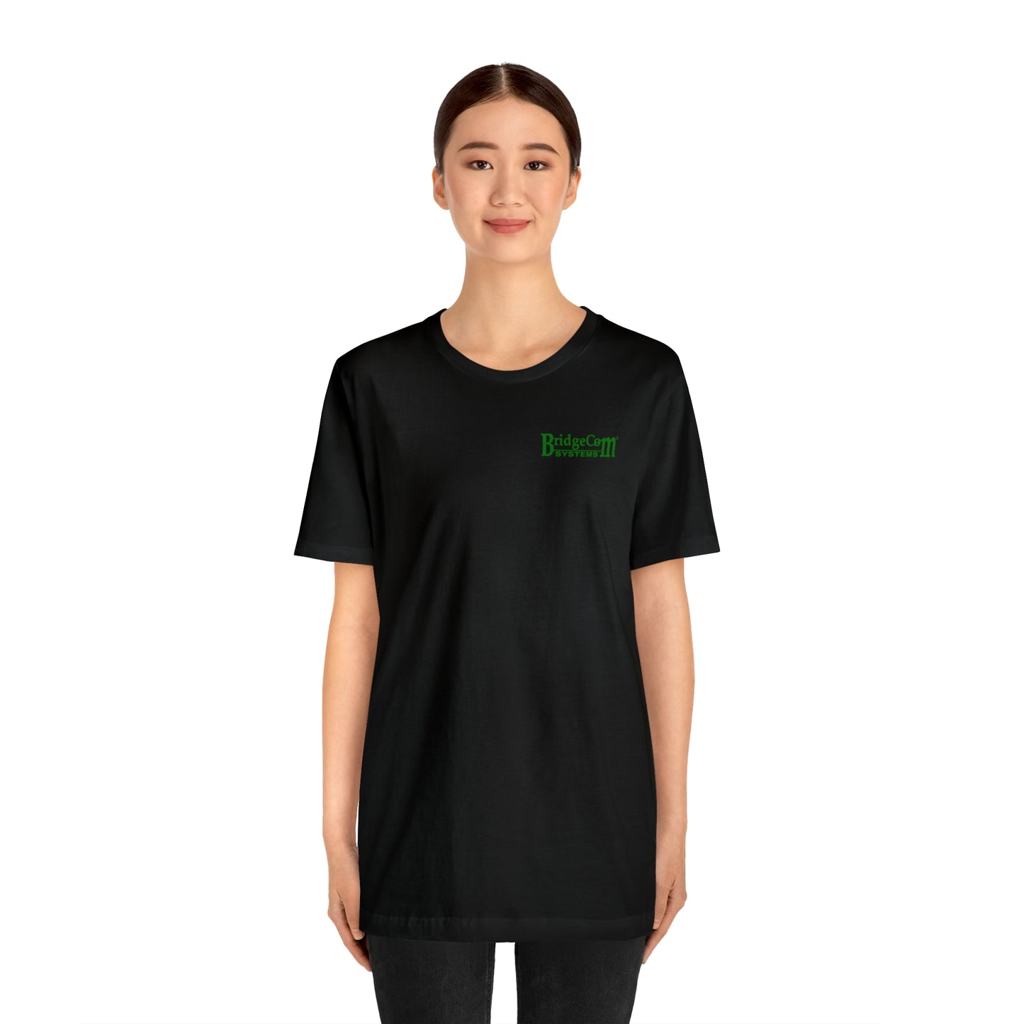 A person with a neat bun hairstyle is standing and smiling, wearing the Short Sleeve Tee - Small Logo, which is made of black Airlume cotton and features green text that reads "BridesCam of Destruction" on the front. The background is plain white.