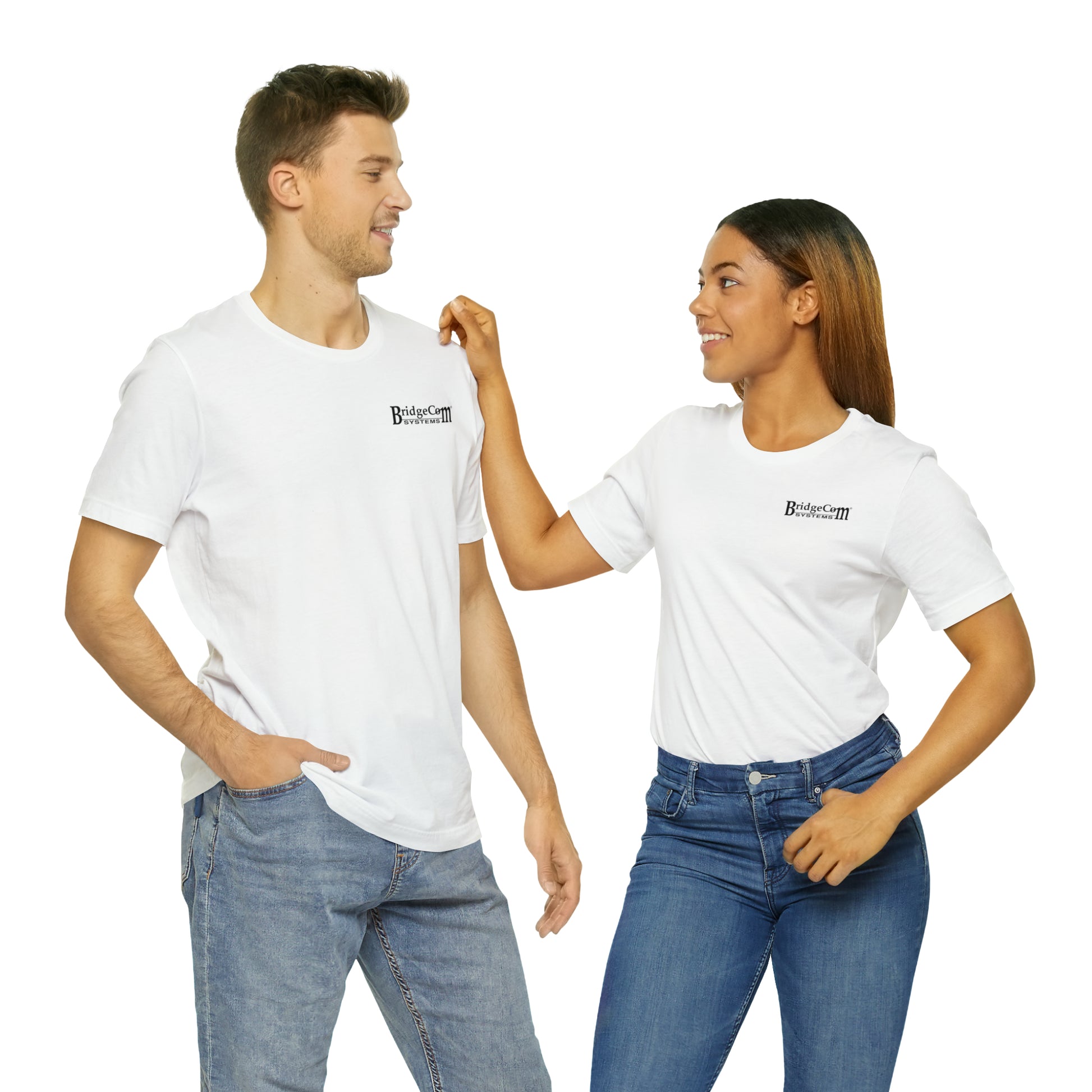 A man and a woman are set against a white backdrop, smiling at each other. They’re both wearing Short Sleeve Tees with small logos made from 100% Airlume cotton, paired with blue jeans. The woman has her right hand gently raised towards the man's shoulder, highlighting the comfort of BridgeCom Systems' apparel.