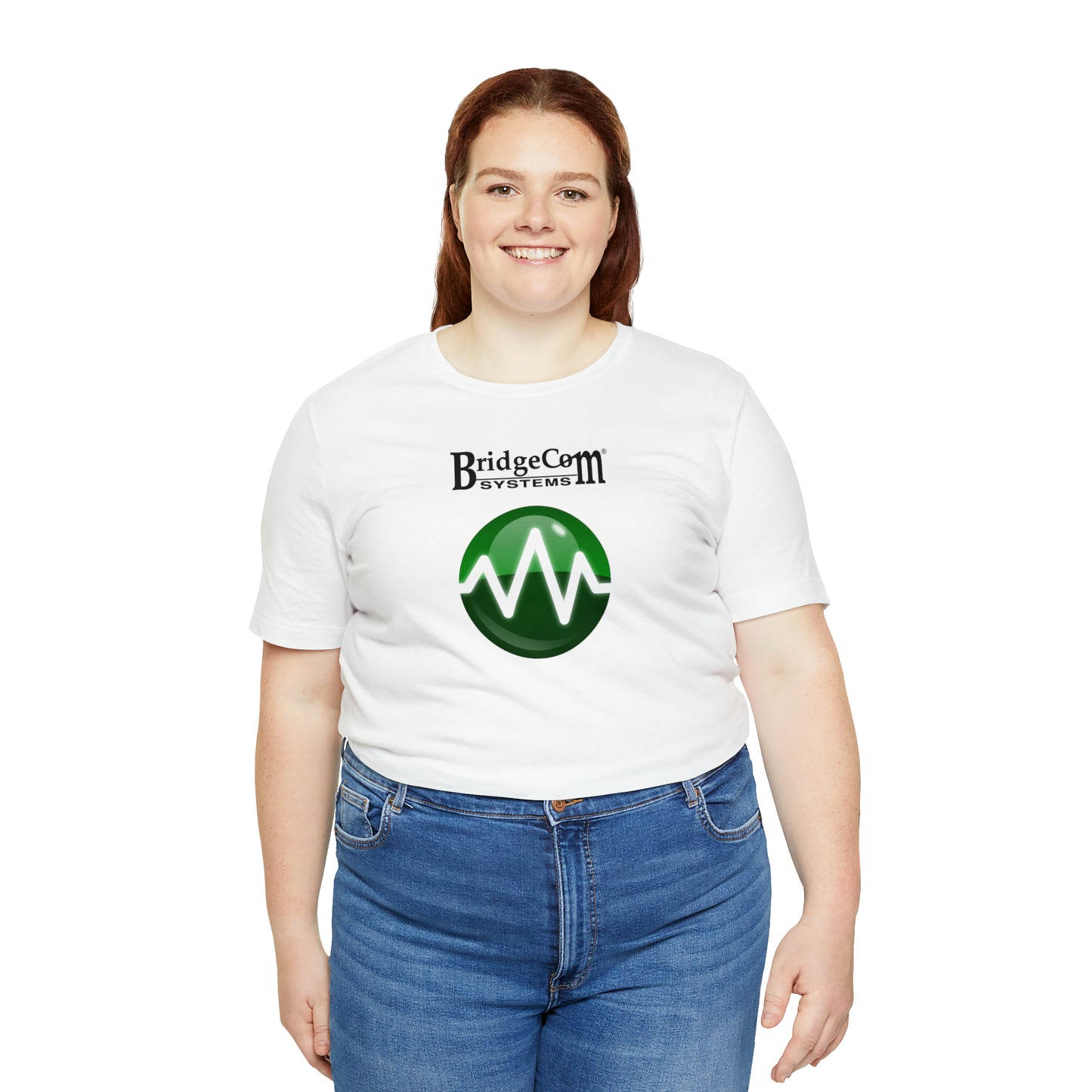 A person sporting a white Unisex Short Sleeve BridgeCom Tee - Alternate Logo featuring "BridgeCom Systems" and a green circular design stands against a white backdrop. They have shoulder-length red hair, are smiling at the camera, and are wearing blue jeans.