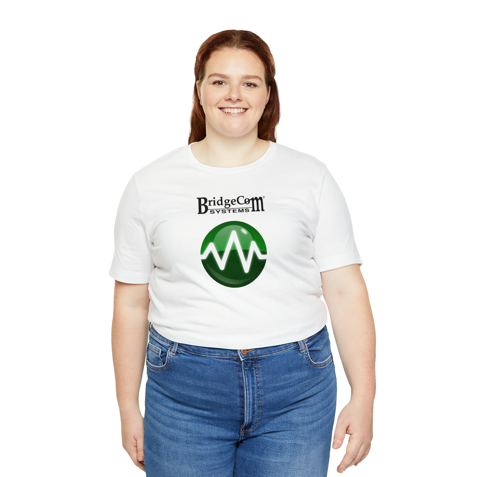 A person sporting a white Unisex Short Sleeve BridgeCom Tee - Alternate Logo featuring "BridgeCom Systems" and a green circular design stands against a white backdrop. They have shoulder-length red hair, are smiling at the camera, and are wearing blue jeans.