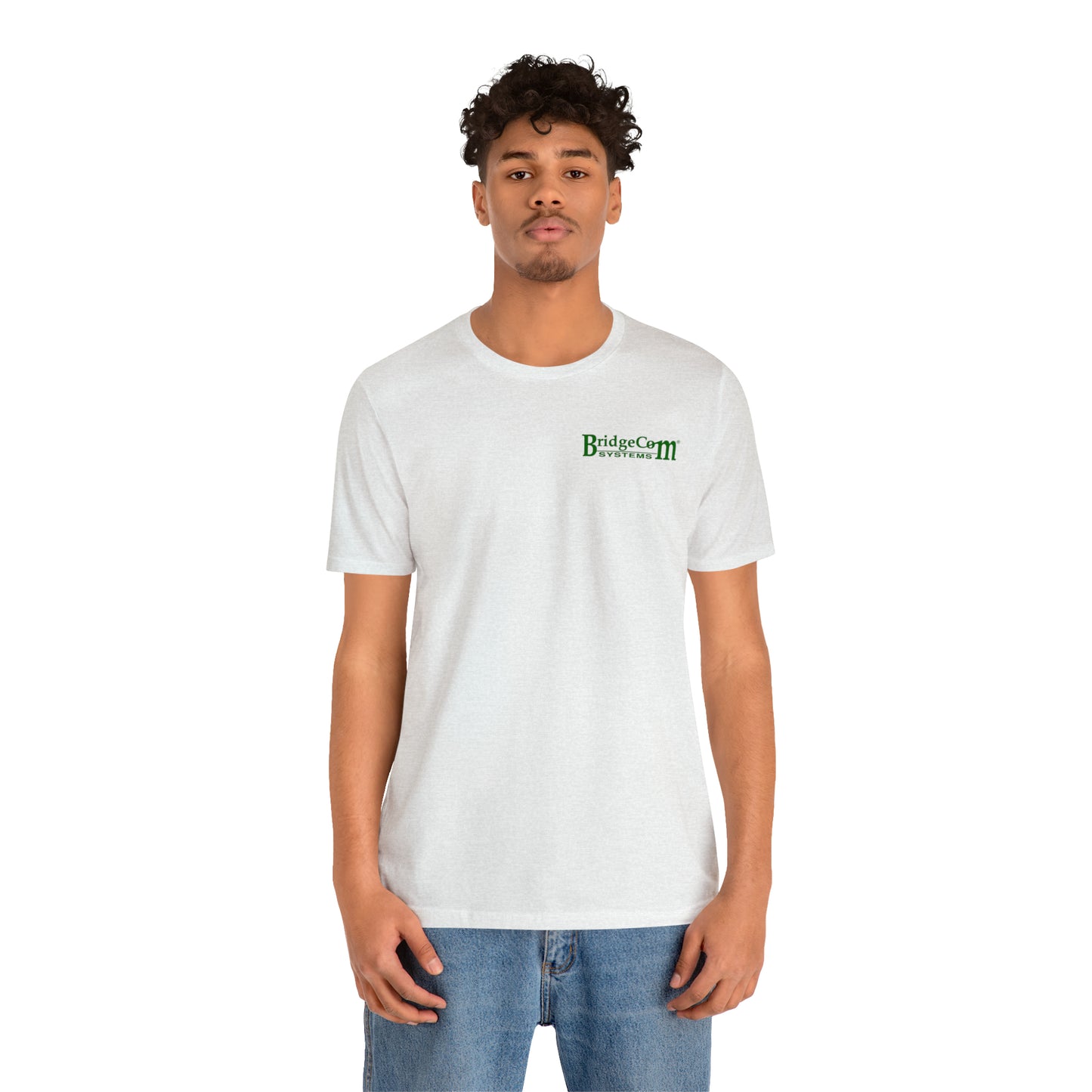 A person with curly hair and a light beard stands facing the camera, wearing a plain white Short Sleeve Tee - Small Logo from BridgeCom Systems, made from 100% Airlume combed and ringspun cotton, paired with blue jeans. The background is plain white.