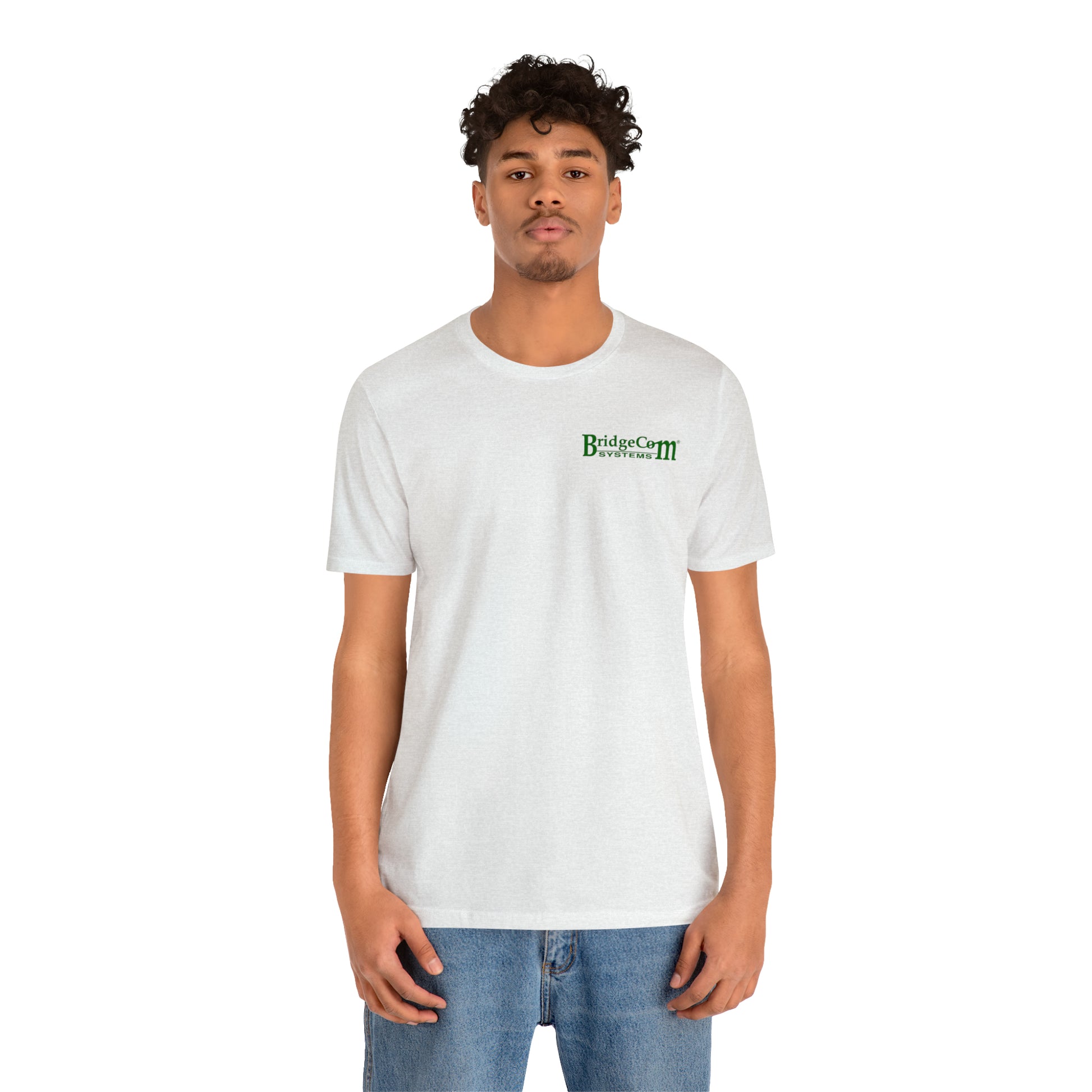 A person with curly hair and a light beard stands facing the camera, wearing a plain white Short Sleeve Tee - Small Logo from BridgeCom Systems, made from 100% Airlume combed and ringspun cotton, paired with blue jeans. The background is plain white.