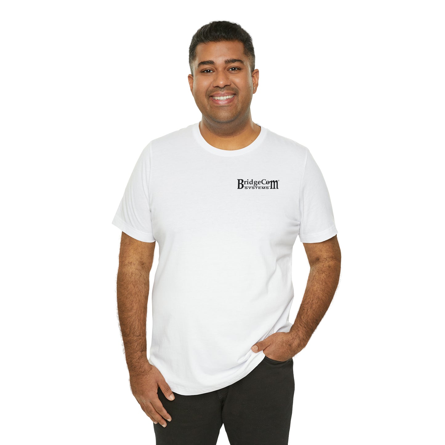 A smiling person stands against a plain white background wearing the Short Sleeve Tee - Small Logo with the BridgeCom Systems logo printed on the left chest. They have one hand in their pocket and appear relaxed and casual.