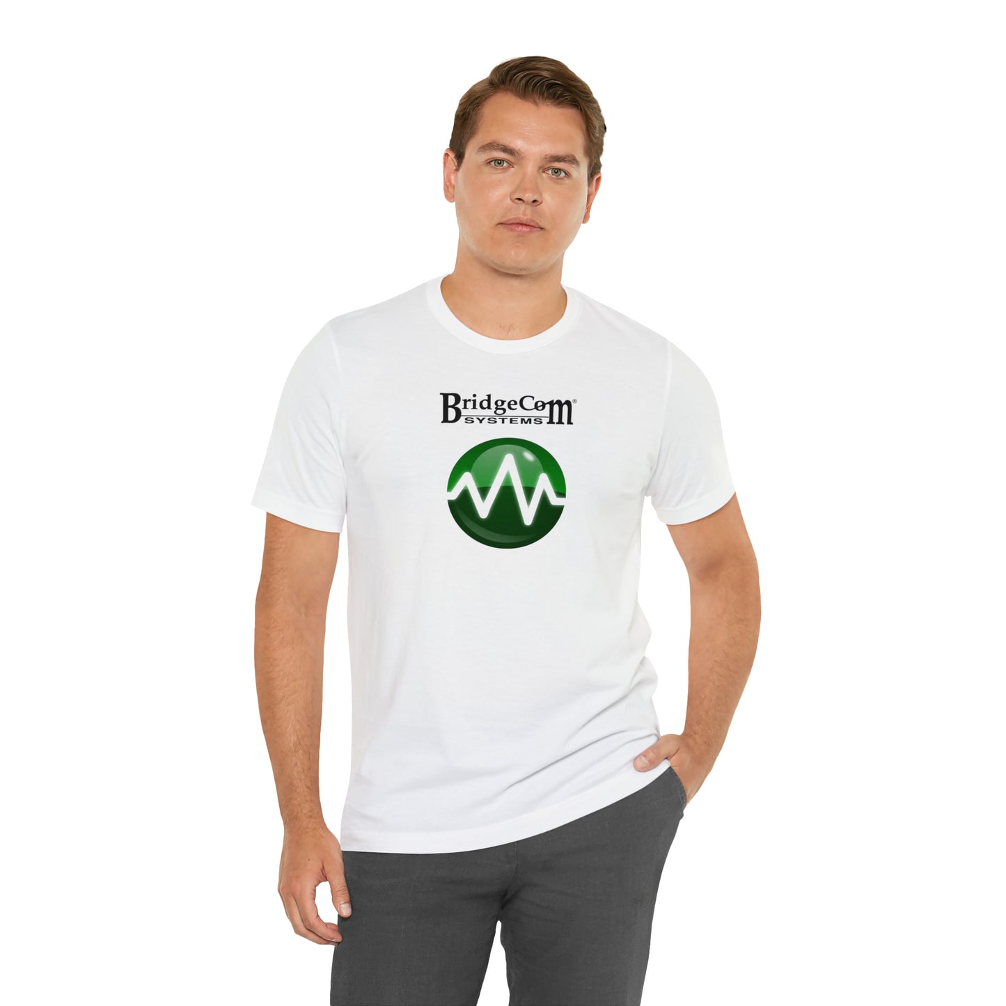 A man with short hair is standing against a white background, wearing a Unisex Short Sleeve BridgeCom Tee - Alternate Logo featuring the "BridgeCom Systems" logo and a green circular emblem underneath. Made from Airlume cotton, it complements his relaxed pose as he looks at the camera with one hand in his pocket.
