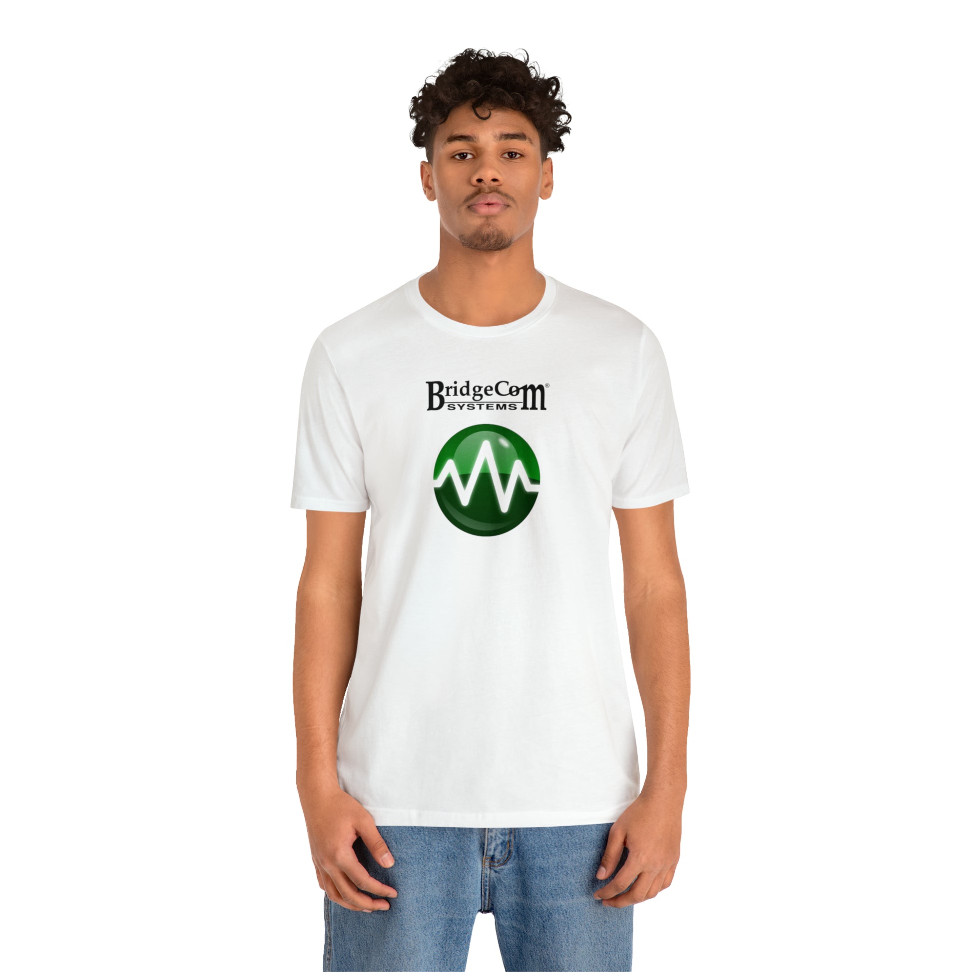 A person with short curly hair is standing against a plain white background, wearing a Unisex Short Sleeve BridgeCom Tee - Alternate Logo made of soft Airlume cotton, featuring the "BridgeCom Systems" logo and a green circle with a stylized white waveform. They are also wearing blue jeans.