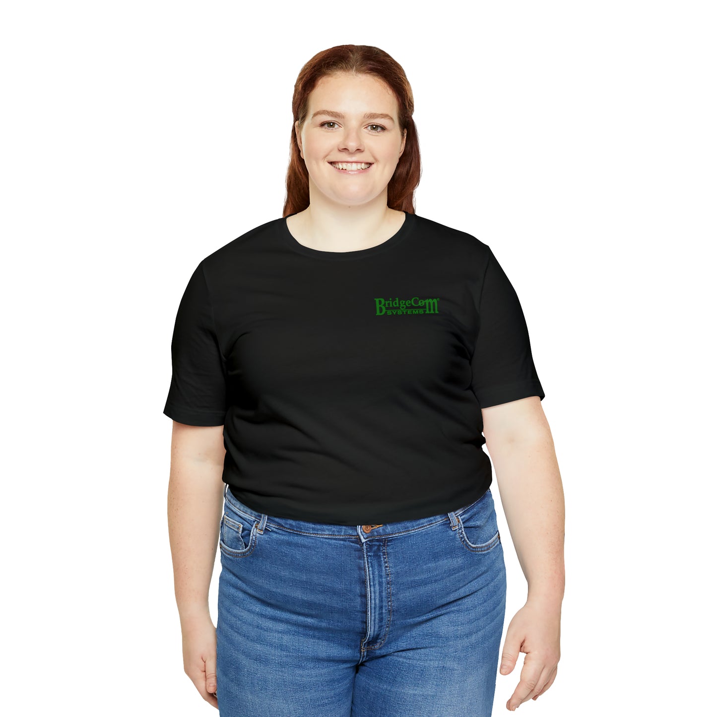 A person with long, brown hair is smiling and facing forward. They are wearing a black Short Sleeve Tee - Small Logo made of Airlume combed and ringspun cotton, featuring the green "BridgeCom University" logo on the left side of the chest. Paired with blue jeans, they stand against a plain white background.