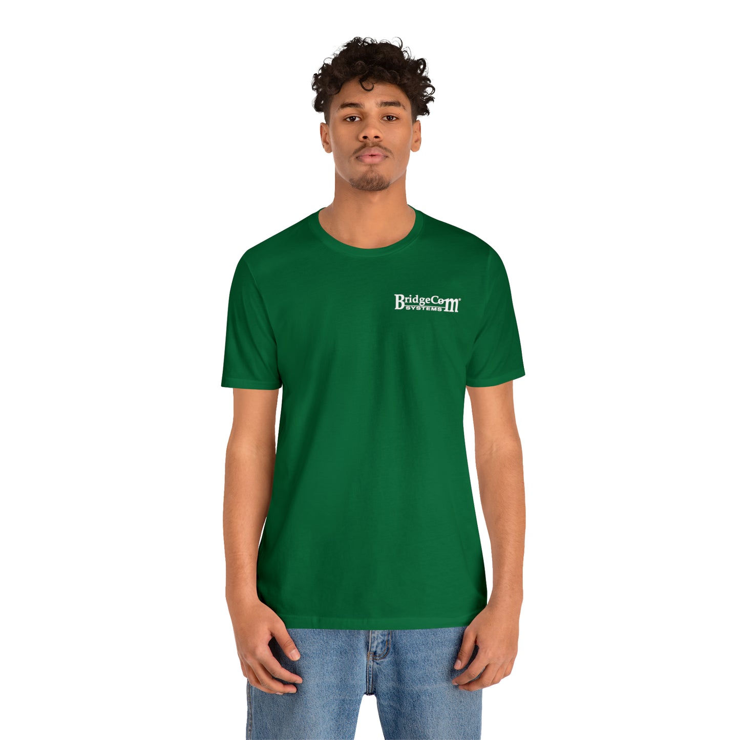 A person with short curly hair is standing and facing forward against a plain white background. They are wearing the "Short Sleeve Tee - Small Logo" in green, made from Airlume combed cotton, featuring a small white "BridgeCom Systems III" logo on the upper left side, paired with blue jeans.