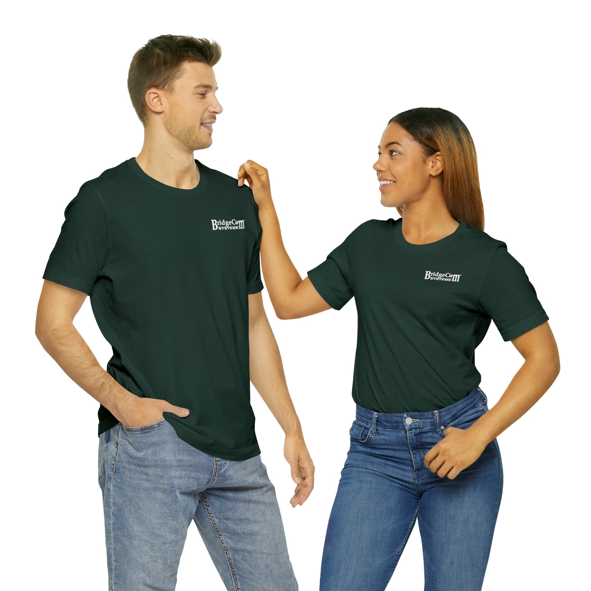 A man and a woman are standing side by side, both clad in matching green Short Sleeve Tees - Small Logo and blue jeans. The man has his hand in his pocket, and the woman is smiling while touching his shoulder. Their white BridgeCom Systems logos on the left chest highlight their shared communication.