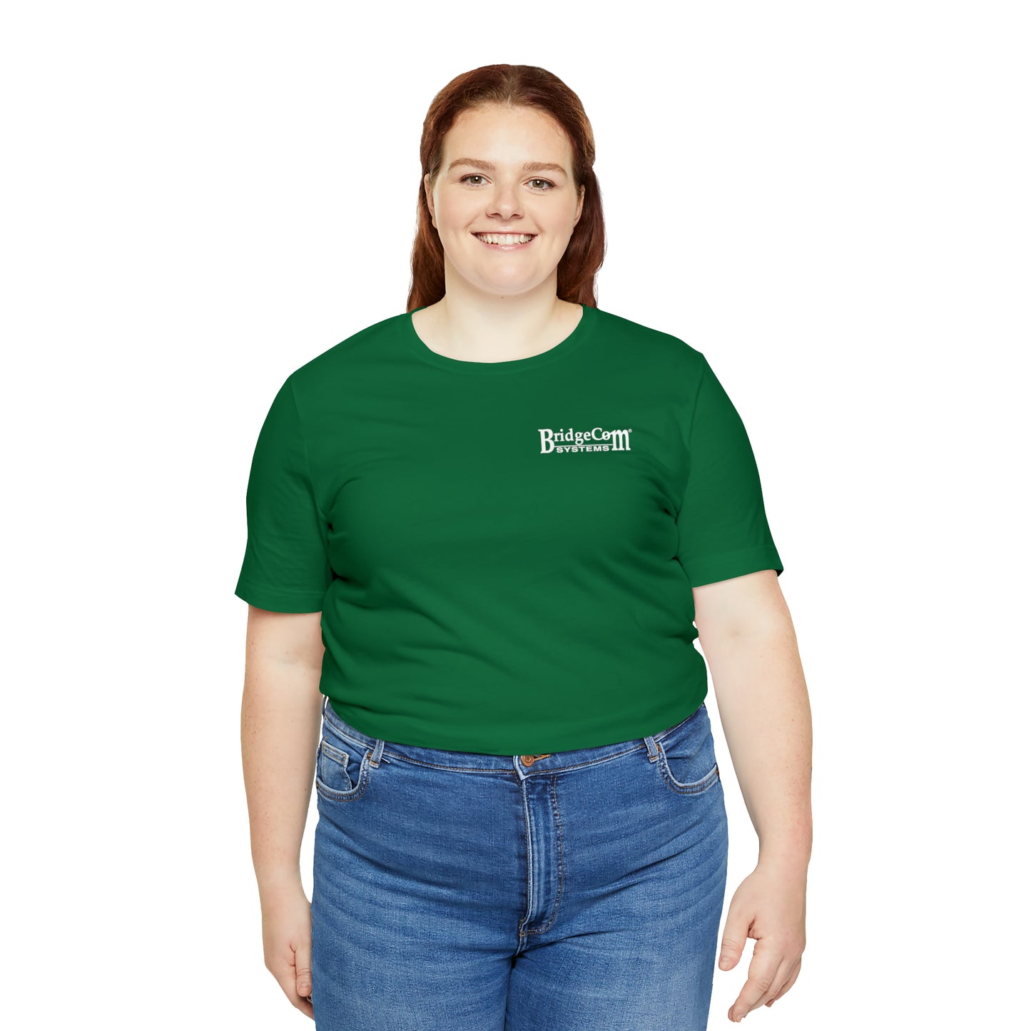 A woman with long brown hair is smiling and wearing a green Short Sleeve Tee - Small Logo from BridgeCom Systems, made from Airlume combed cotton. She pairs it with blue jeans and stands against a plain white background, radiating both comfort and communication prowess.