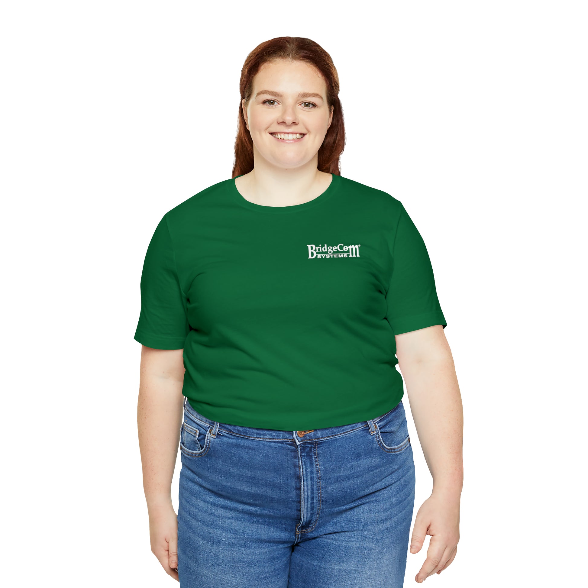 A woman with long brown hair is smiling and wearing a green Short Sleeve Tee - Small Logo from BridgeCom Systems, made from Airlume combed cotton. She pairs it with blue jeans and stands against a plain white background, radiating both comfort and communication prowess.