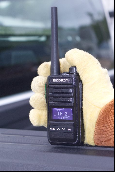 A gloved hand holds a black BridgeCom MV-65 License FREE Walkie Talkie, its display showing "CH 2" and several buttons below the screen.