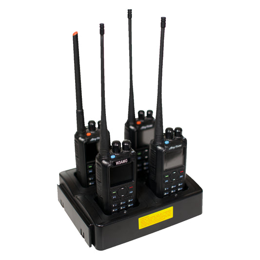 A Four Slot AnyTone 868/878 Rapid Gang Charger holding four black AnyTone 868-878 two-way radios with long antennas. Each radio features a small screen, buttons, and a speaker grille. The black charging base, ideal for an amateur radio club, has a yellow label on the front.