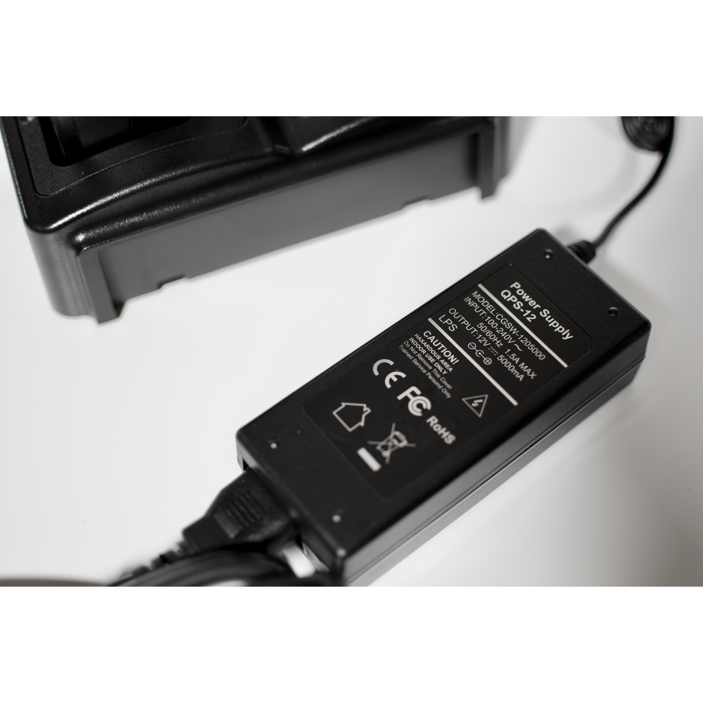 A black Four Slot AnyTone 868/878 Rapid Gang Charger connected to an electronic device from the AnyTone 868-878 series. The label includes safety information, voltage ratings, and various certification marks. Perfect for amateur radio club enthusiasts, it can charge four HT's simultaneously on a white surface.