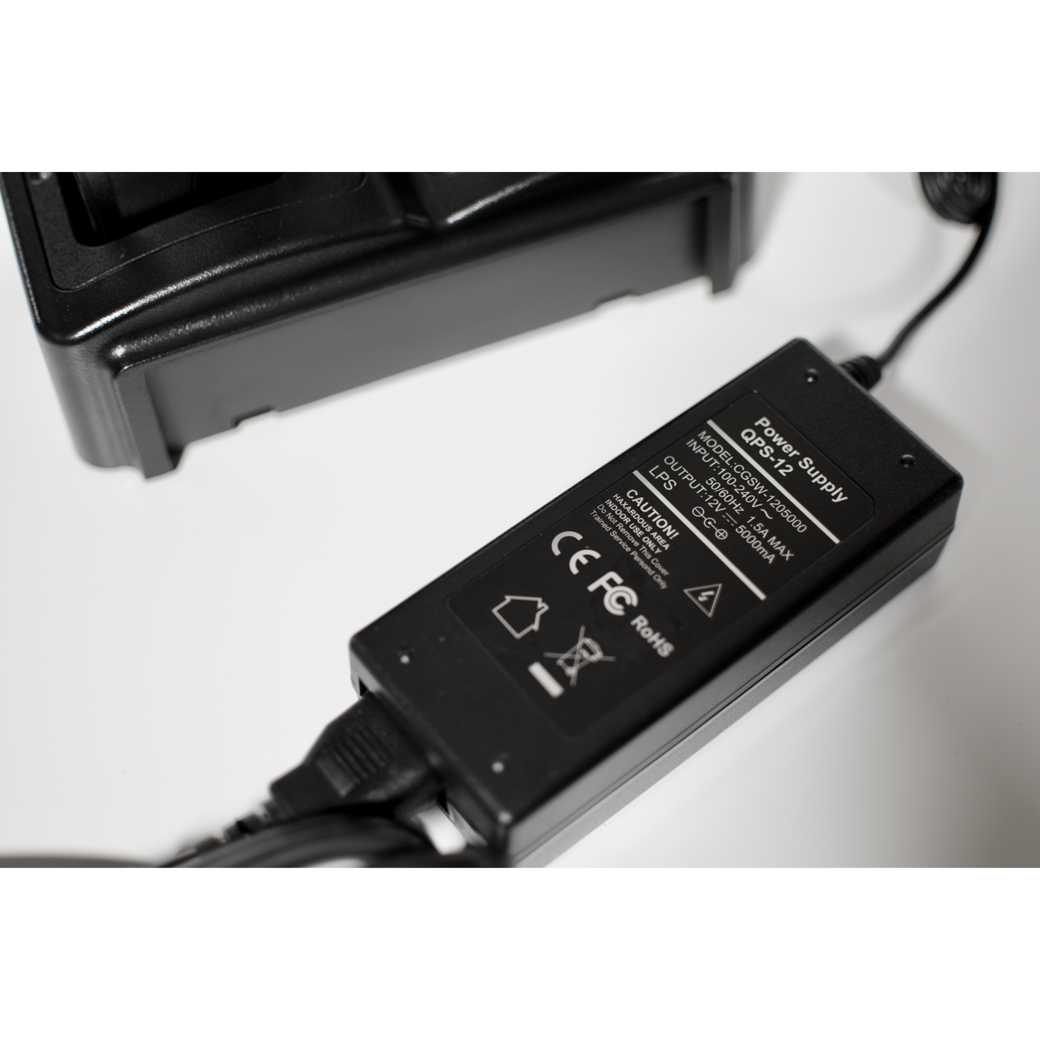 A black Four Slot AnyTone 868/878 Rapid Gang Charger connected to an electronic device from the AnyTone 868-878 series. The label includes safety information, voltage ratings, and various certification marks. Perfect for amateur radio club enthusiasts, it can charge four HT's simultaneously on a white surface.