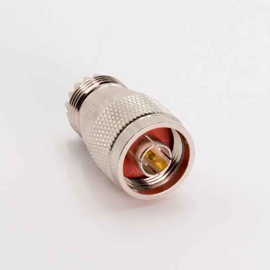 A detailed view of an N Male to UHF Female Adapter featuring a knurled grip and a threaded end. The center pin is clearly visible from the front, encircled by red insulating material. Positioned against a plain white background, the adapter highlights its precision design characteristic of high-quality coax adapters.