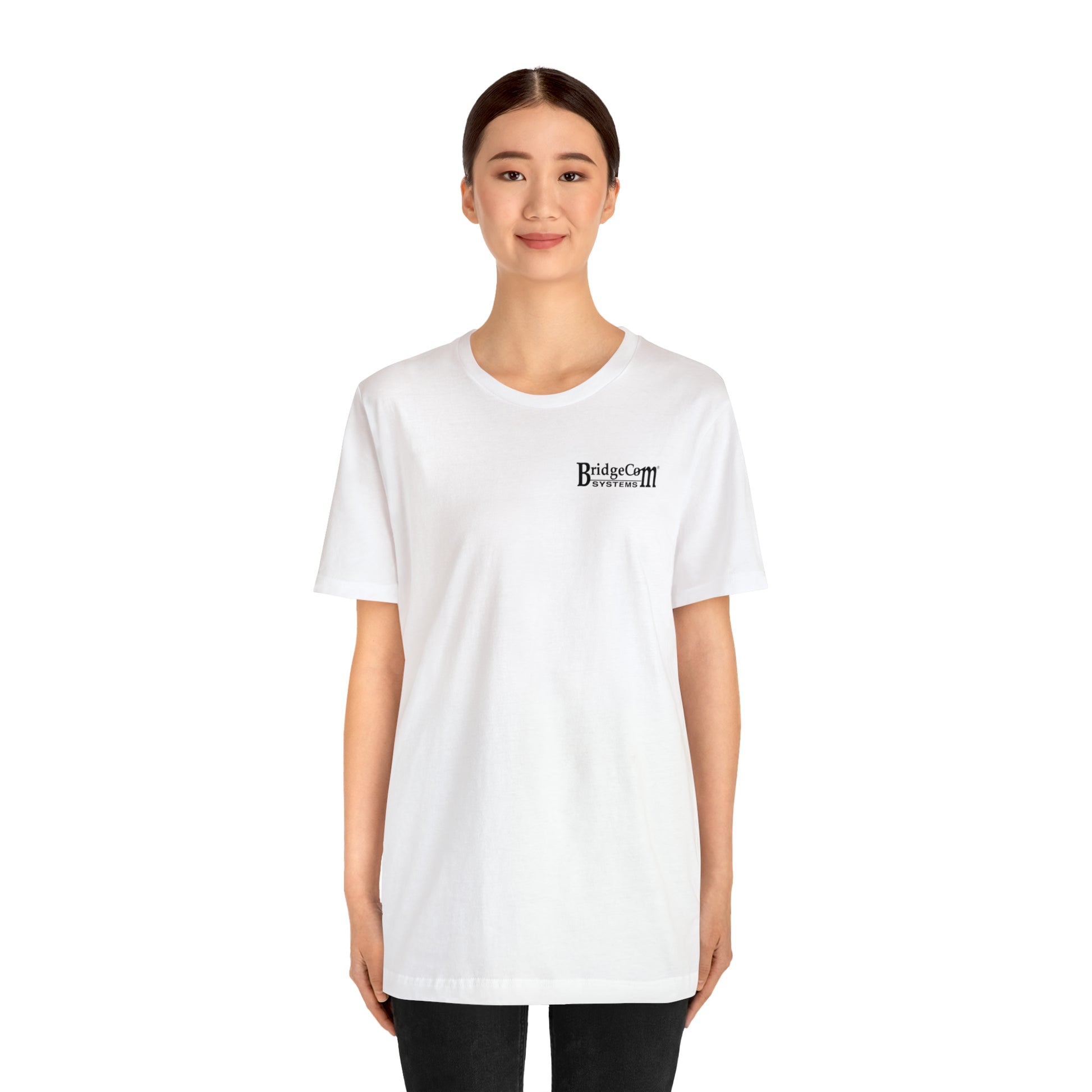 A person stands facing forward, wearing a Short Sleeve Tee - Small Logo made of Airlume combed cotton. The T-shirt features the text "Bridges and Camps Divided 1111" on the upper left side. Against a plain white background, the individual with dark hair and a slight smile seems to embody clear communication.