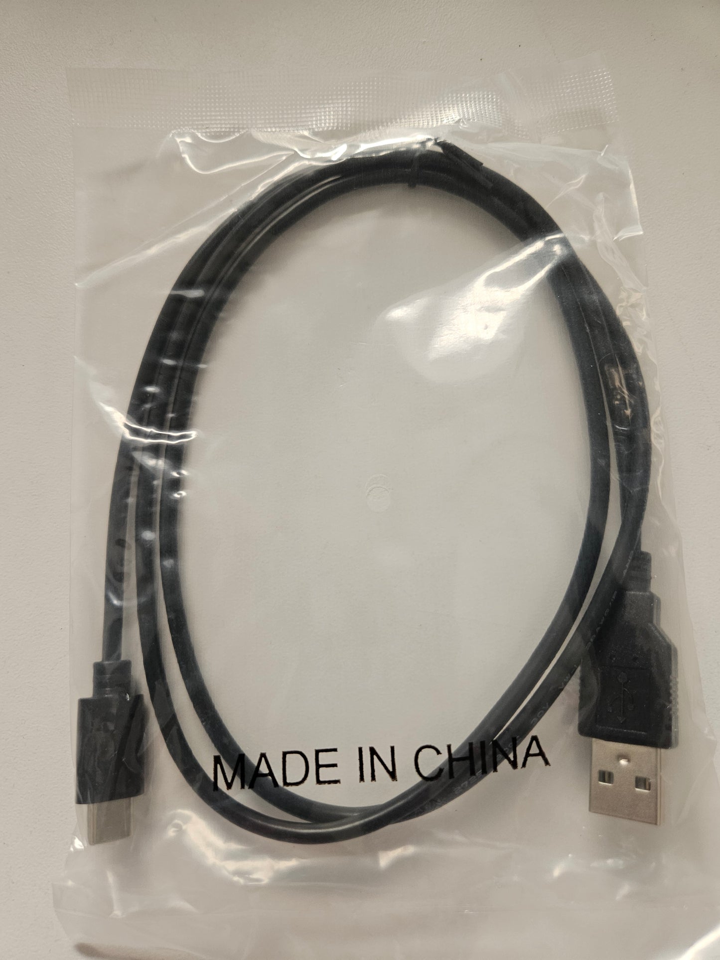 A USB Type A to USB Type C cable in black is packaged in a clear plastic bag labeled "MADE IN CHINA" and placed on a white surface.