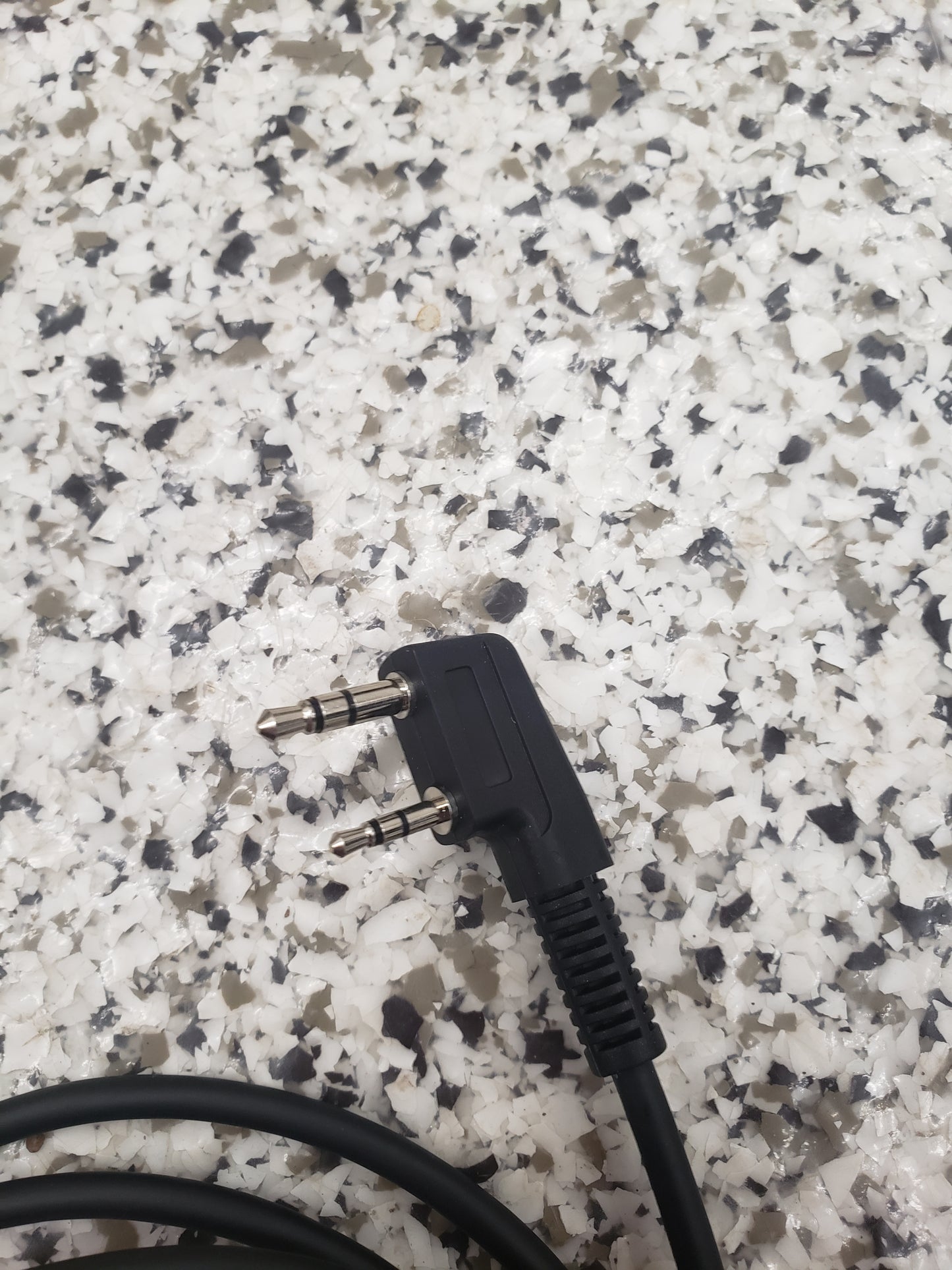 The BridgeCom Buddy Programming Cable, featuring a black dual 3.5mm right-angle audio plug, rests on a speckled gray and white surface—perfect for programming settings on Buddy FRS handheld radios.