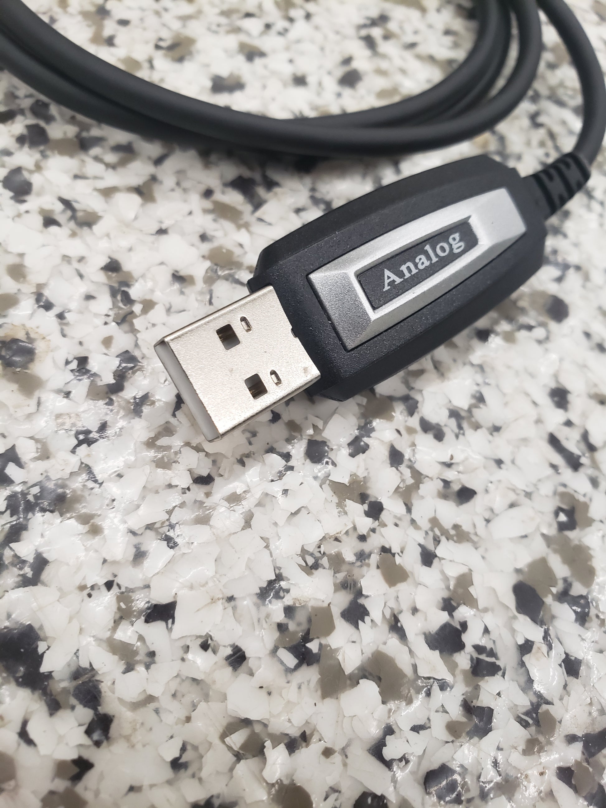A close-up of a BridgeCom Buddy Programming Cable, labeled "Analog," resting on a speckled gray-and-white countertop—perfect for adjusting settings on your Buddy FRS handheld radio.