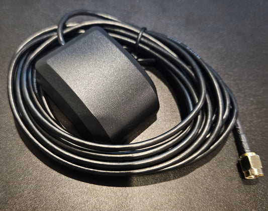 A black rectangular GPS Antenna, designed for compatibility with the AT-D578UV, sits on a dark surface with its attached cable coiled neatly. The cable ends in a small, gold-plated SMA Male connector.