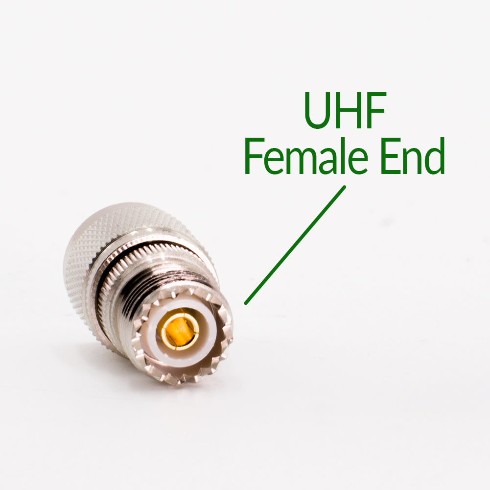 Close-up image of a N Male to UHF Female Adapter. The adapter has a metallic body with a ridged grip for securing attachments, and the inner pin is clearly visible. Green text pointing to the connector reads "UHF Female End." Coax adapters enable this adapter to mate with an N Male connector.